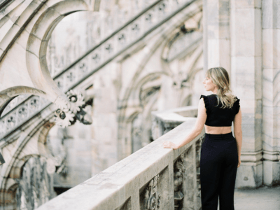 Woman standing on historic balcony looking ahead—symbolizing clarity, reflection, and the choice to live out of your imagination, not your history.