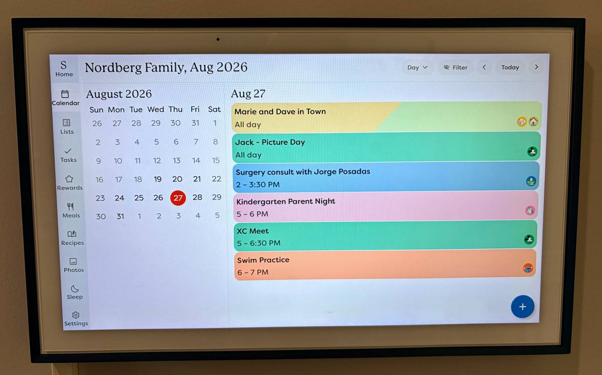 A wall-mounted Skylight Calendar in the Nordberg family's home, showing the daily schedule for August 27 with color-coded events including picture day, a swim practice, and a kindergarten parent night.