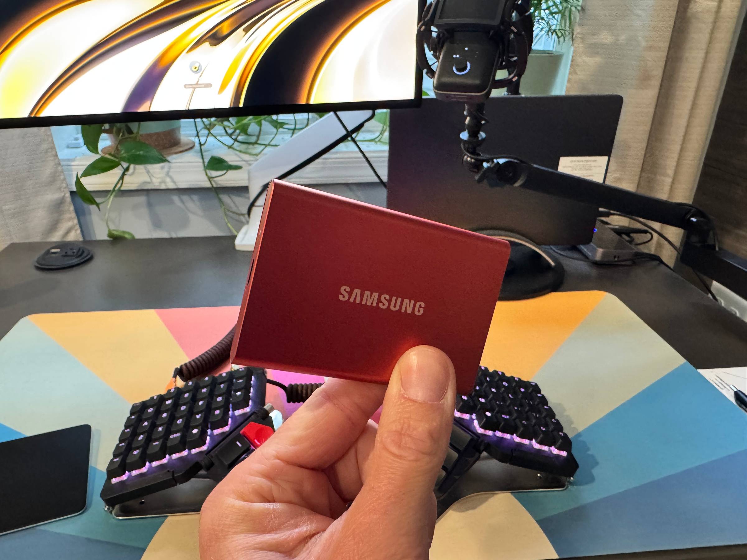 a red Samsung SSD being held in front of a desk and keyboard