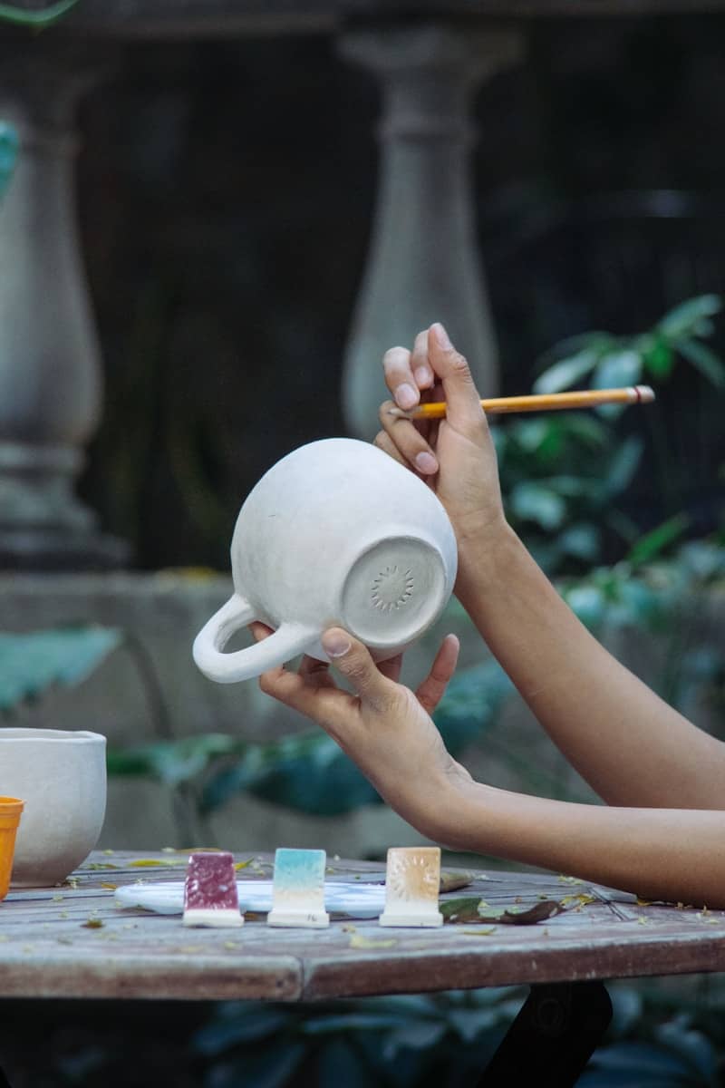 Hands painting a ceramic mug with a pencil