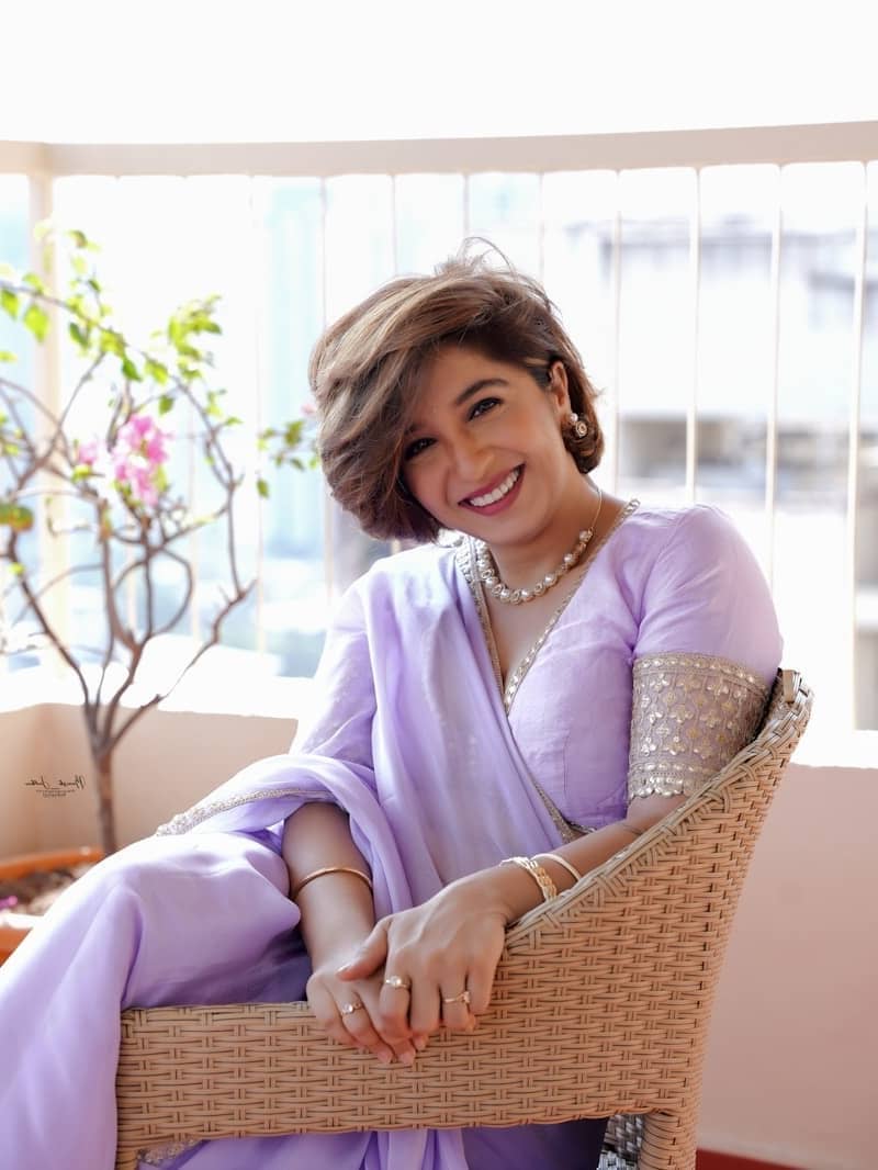 A woman in a purple sari smiles while sitting.