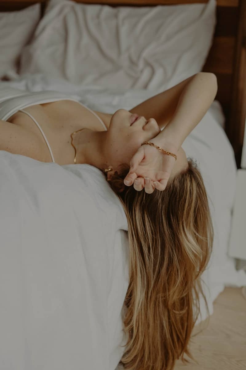 woman in white spaghetti strap top lying on bed