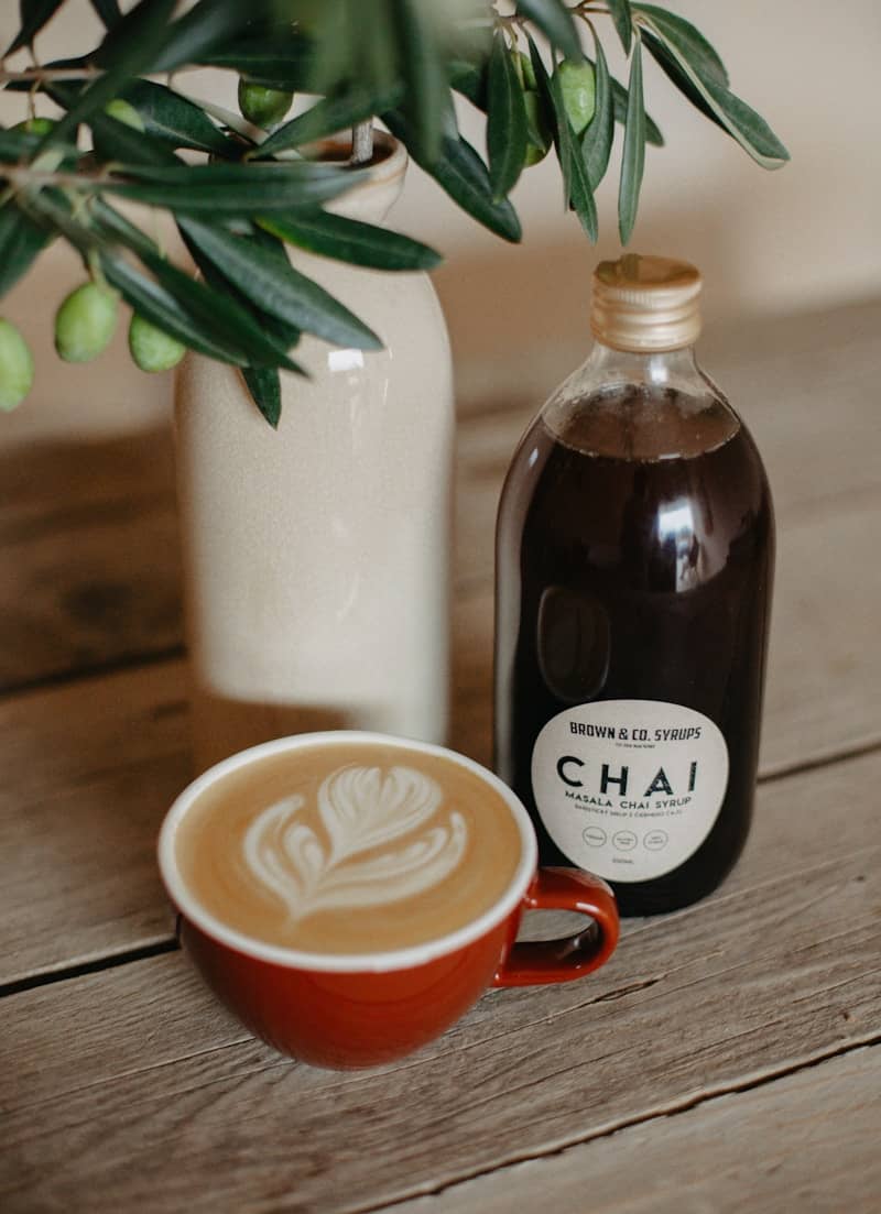 A bottle of chai next to a cup of coffee