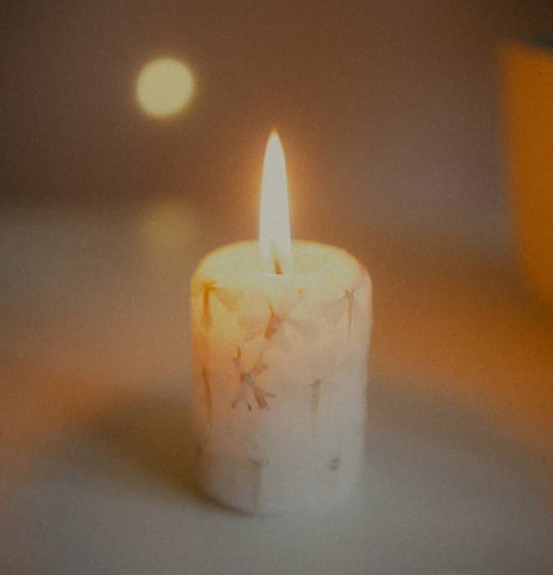 A lit candle with a flame on a blurred background.