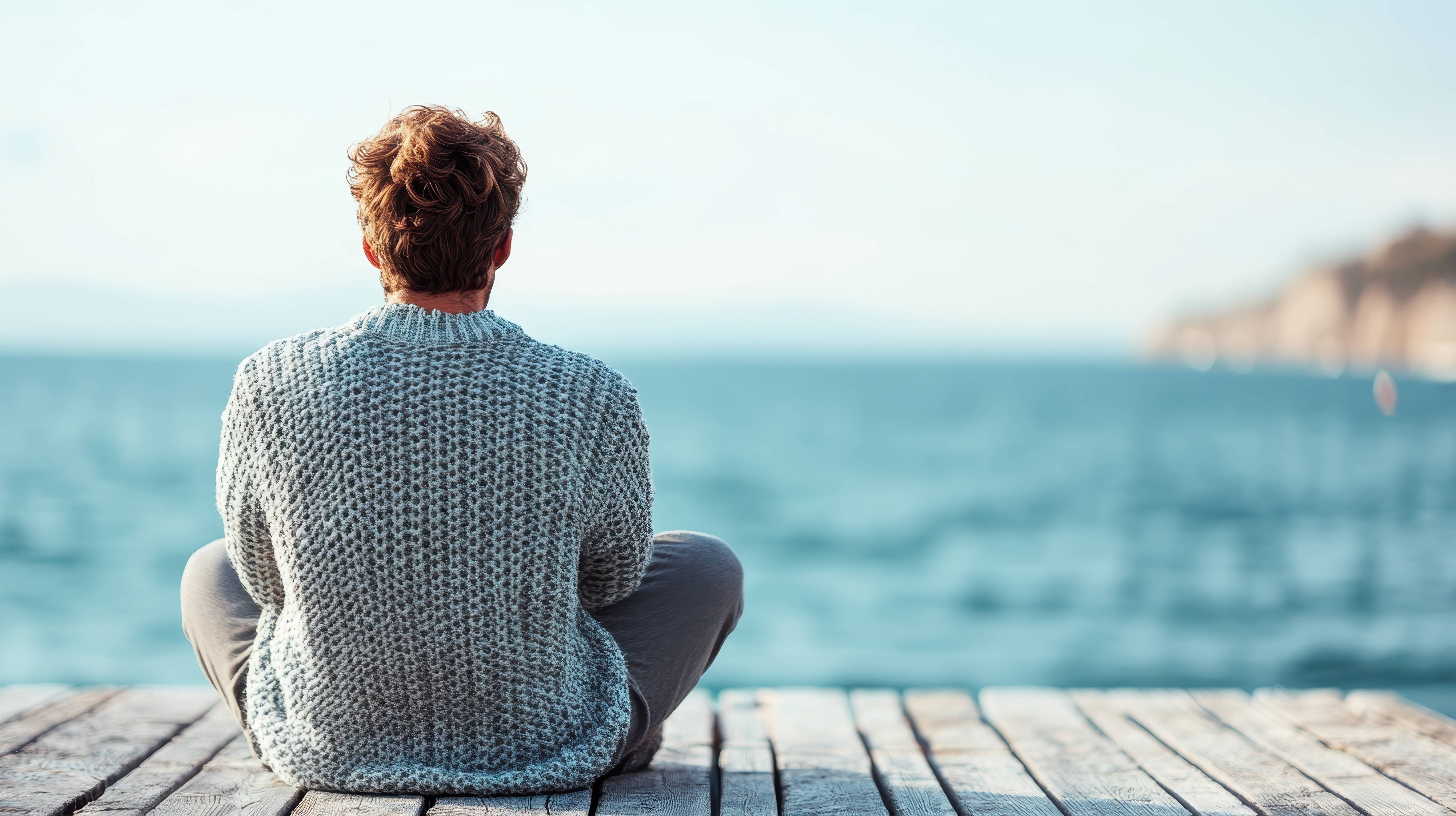 A man sitting on a pier looking out across the water