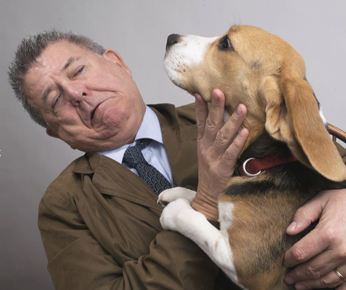 Photo of Tom Ahern with a beagle. The dog has jumped up on him and appears to  try want to lick Tom.