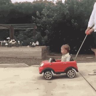 gif of a boy in a stroller appearing jealous of a teddy bear in a remote controlled car
