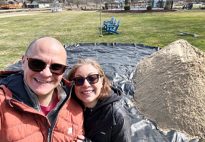 Picture of Brett and Julie in front of a pile of sand in what will be a beachy fire pit