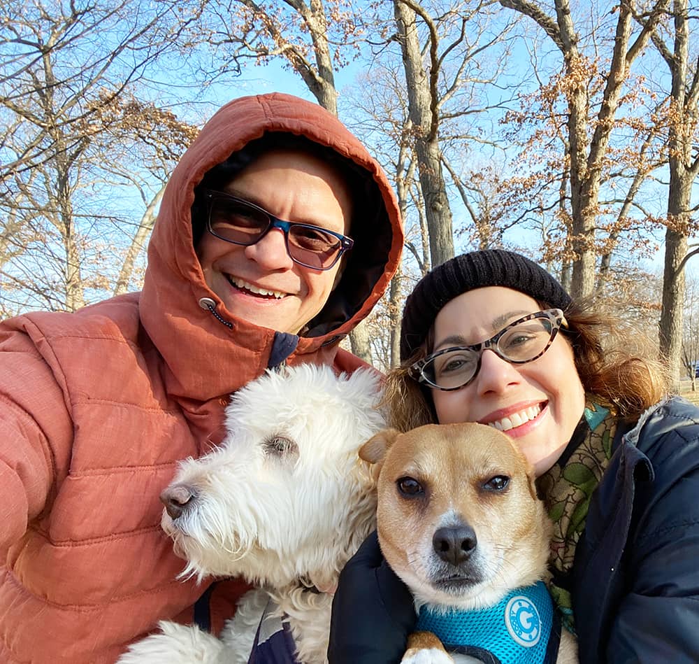Photo of Julie and Brett with their dogs. The humans are wearing coats and hats. The dogs are wearing their harnesses and leads.