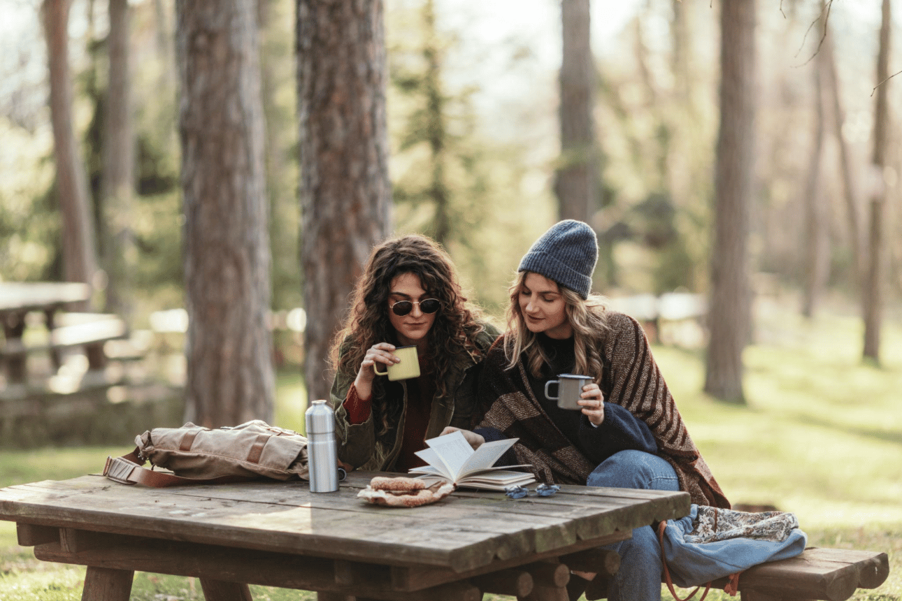 Two friends enjoying a quiet moment together at a picnic table in a wooded setting.