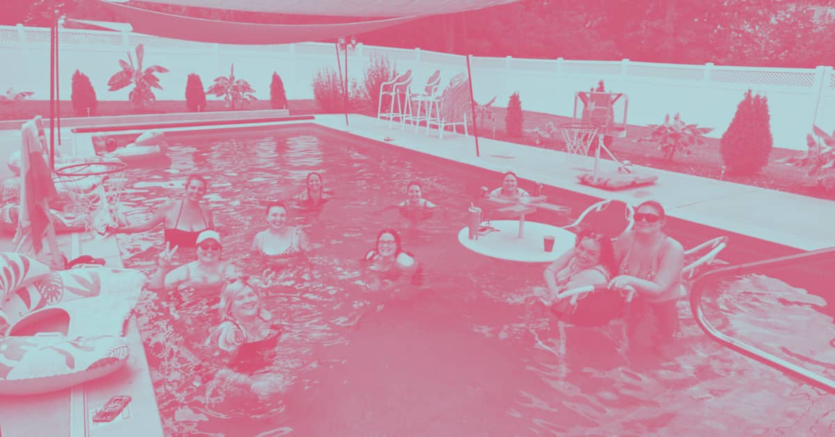 A group of WildKind Collective members smiling together in a backyard swimming pool during a summer gathering.