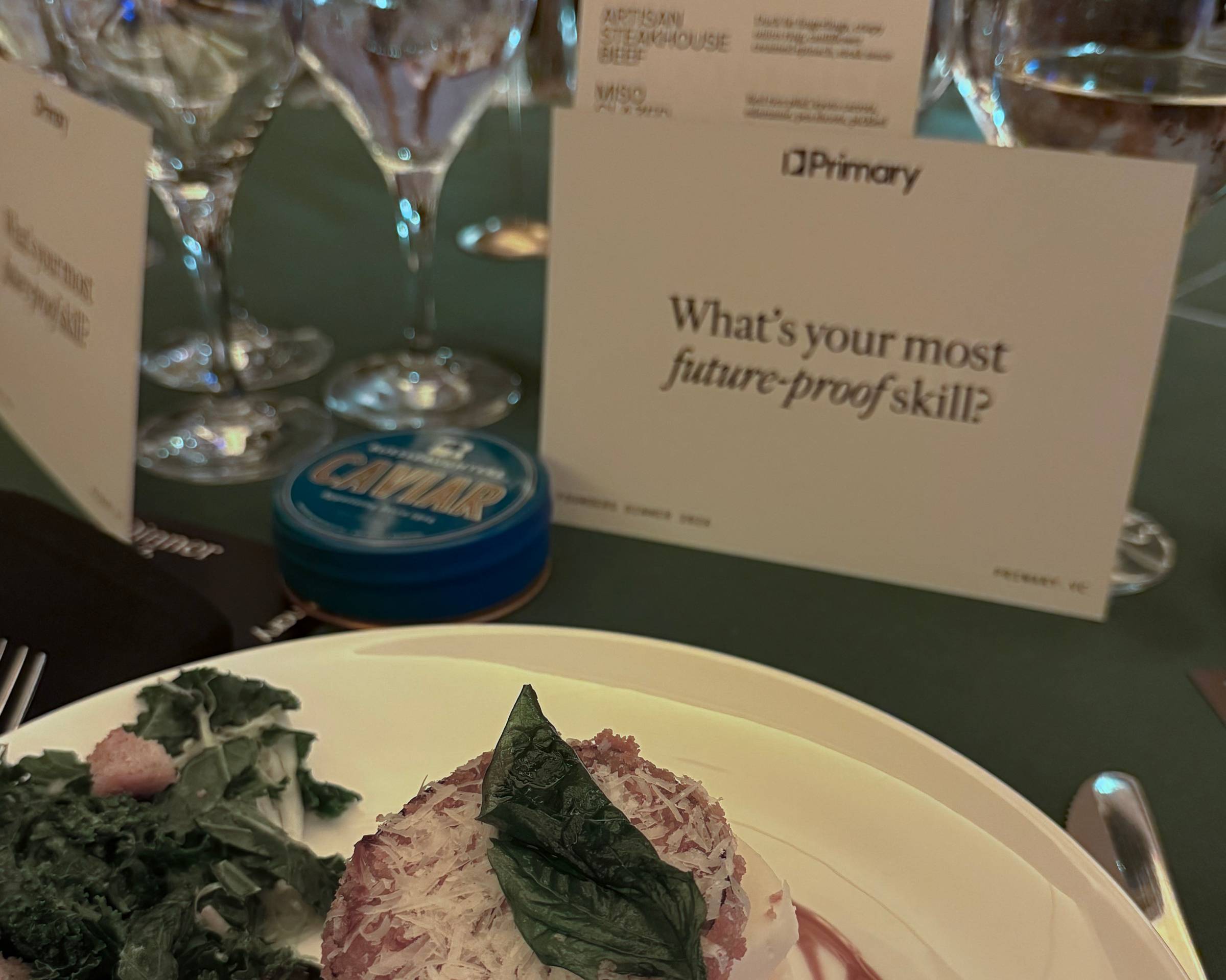 Table setting with a salad, water glasses, and a card printed with "What's your most future proof skill?"