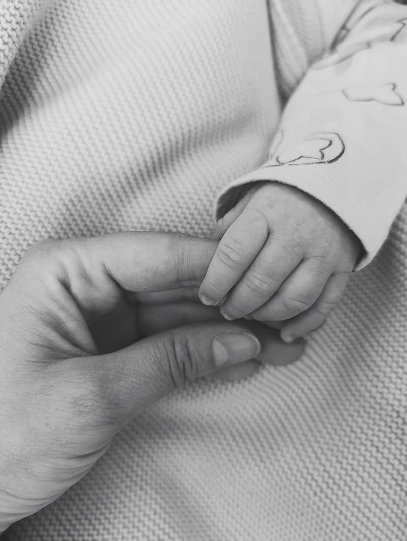 A parent holds their baby's hand.