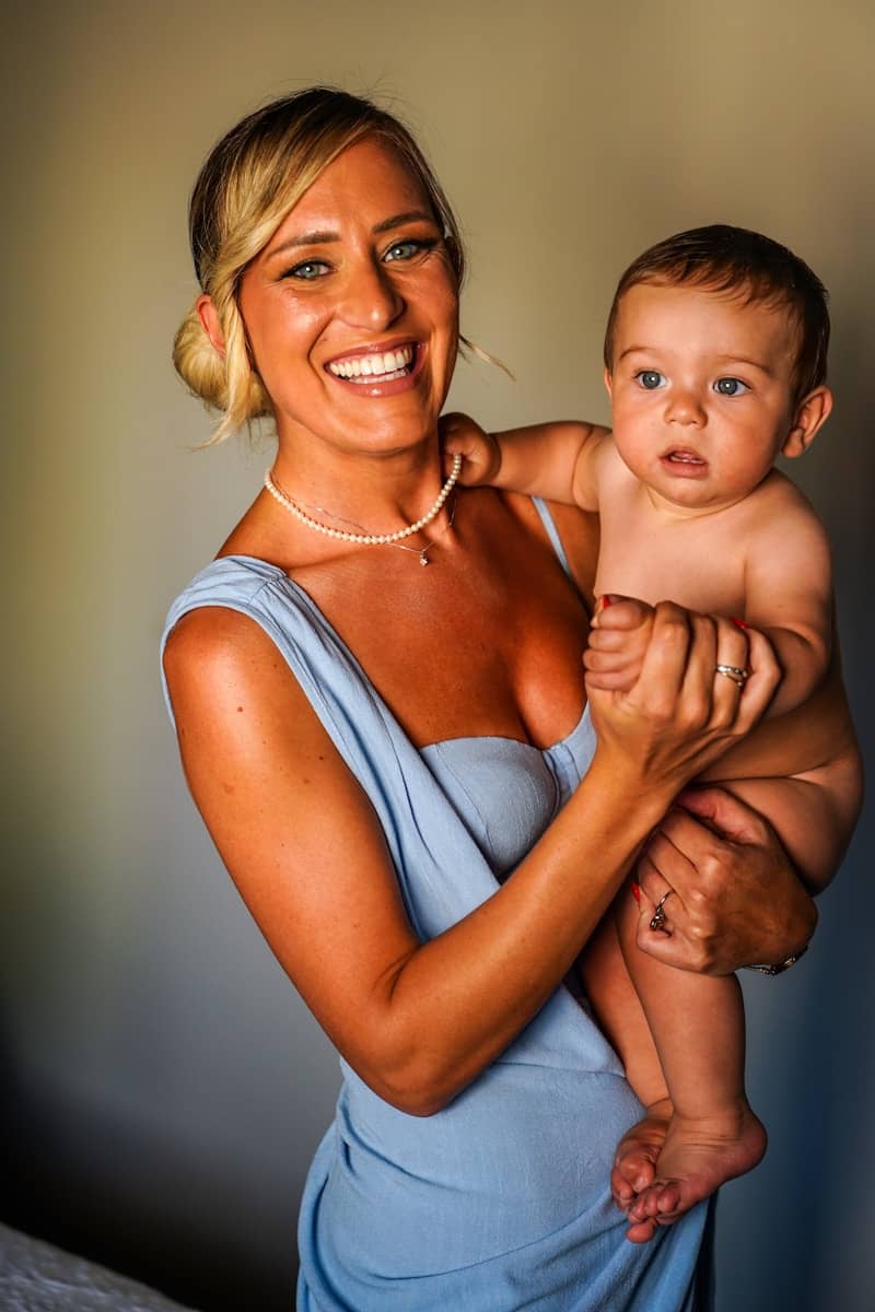 Woman holds a baby, both smiling at the camera.