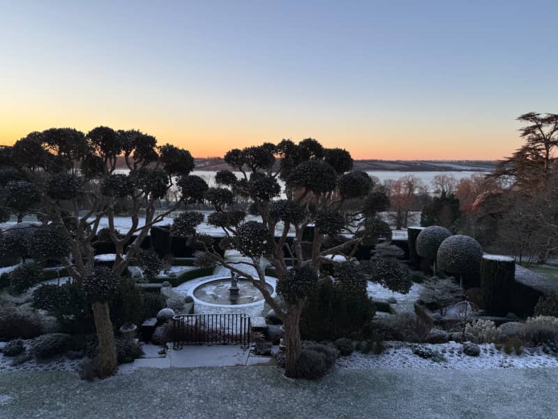 The view over the gardens at Hambleton Hall, with established trees and a fountain in the foreground and Rutland Water in the background