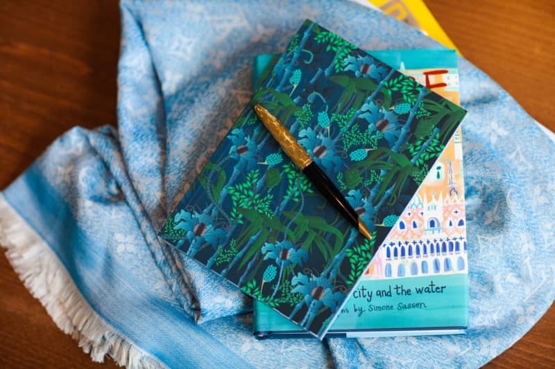 A scarf with a book and a notebook sitting on it, topped with a pen
