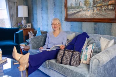 April J Harris sitting on a blue sofa with her feet up. There is a book in herald and her handbag and jacket are alongside her.