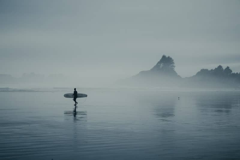 Surfer walks along a misty beach with surfboard