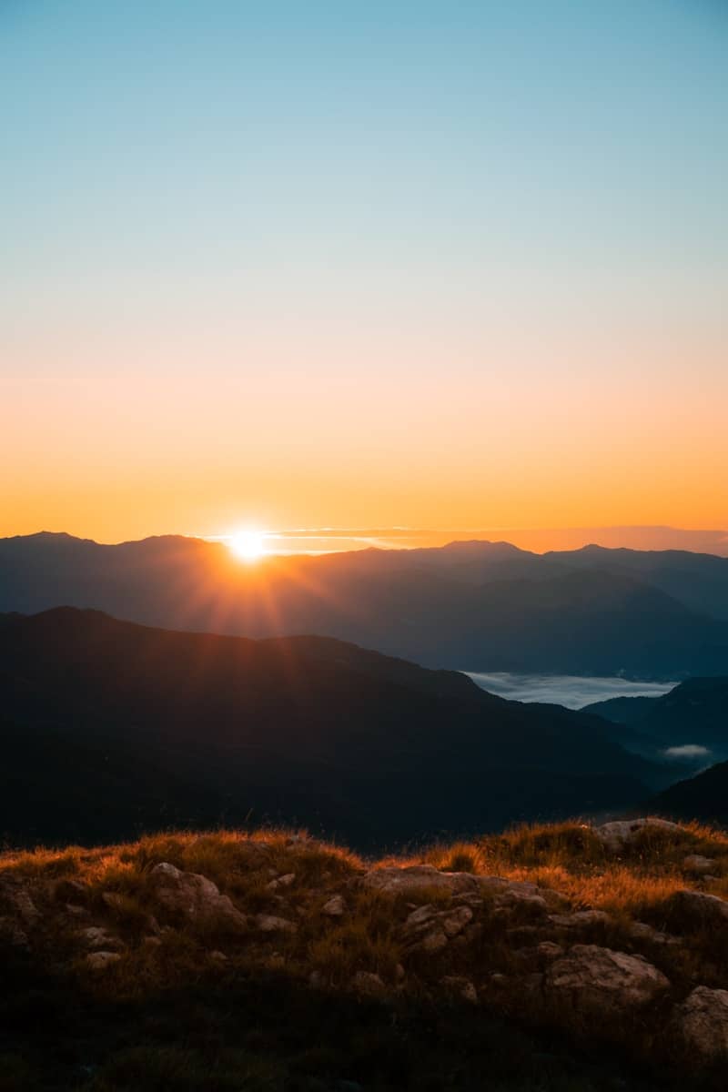 Sunrise over misty mountain ranges with foreground grass.
