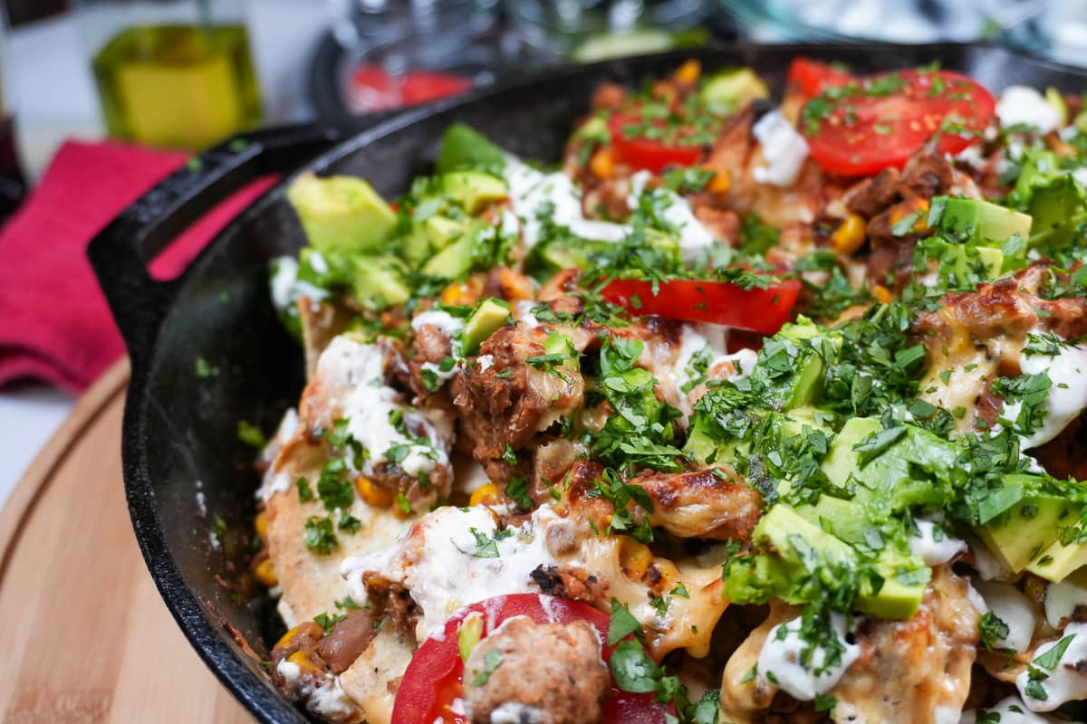 protein packed loaded baked nachos with ground turkey, pinto beans, roasted corn, avocado, tomatoes, Hatch pepper crema and garnished with lime juice and fresh chopped cilantro.