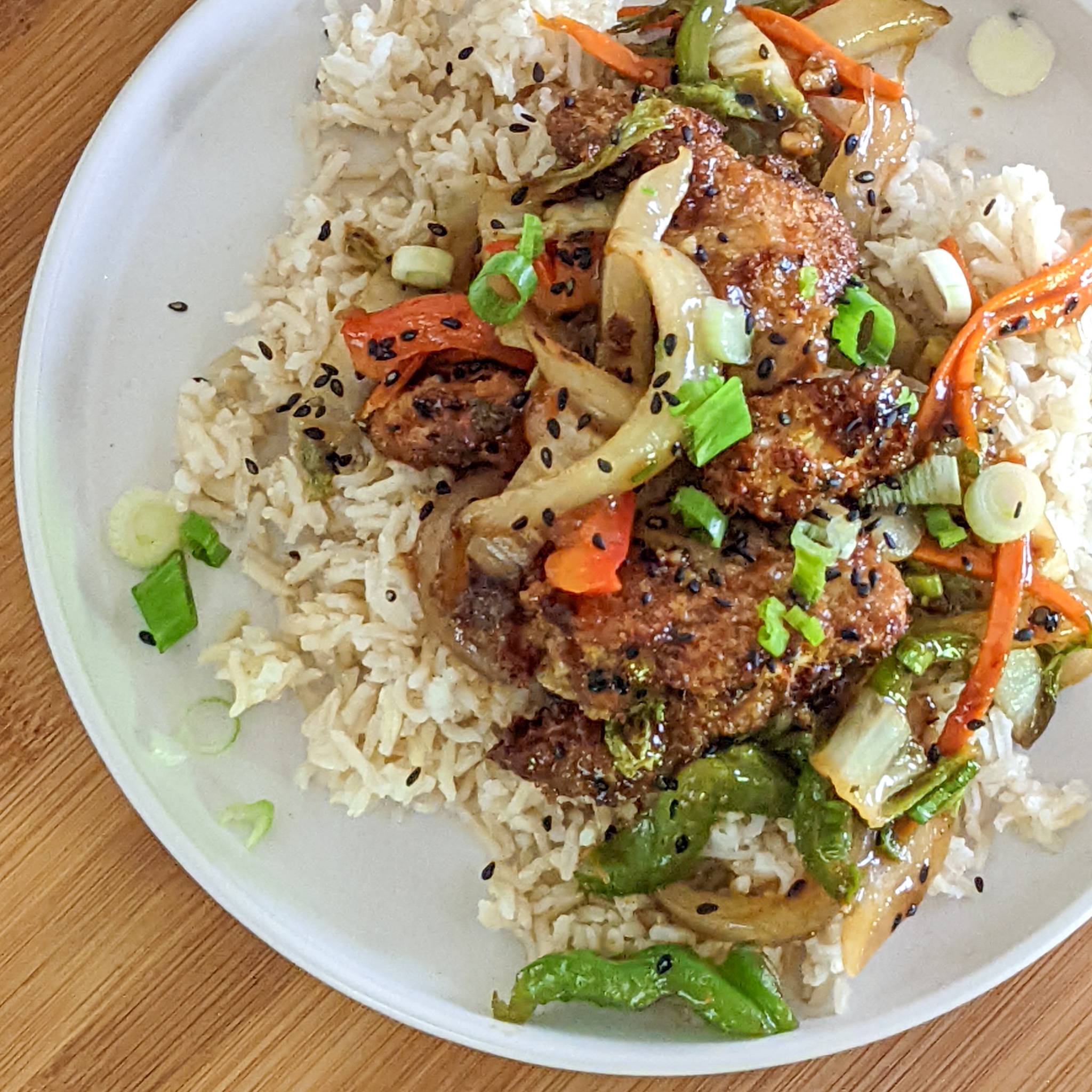 sauce coated crunchy air fried chicken with mixed vegetables on a bed of rice and garnished with black sesame seeds.