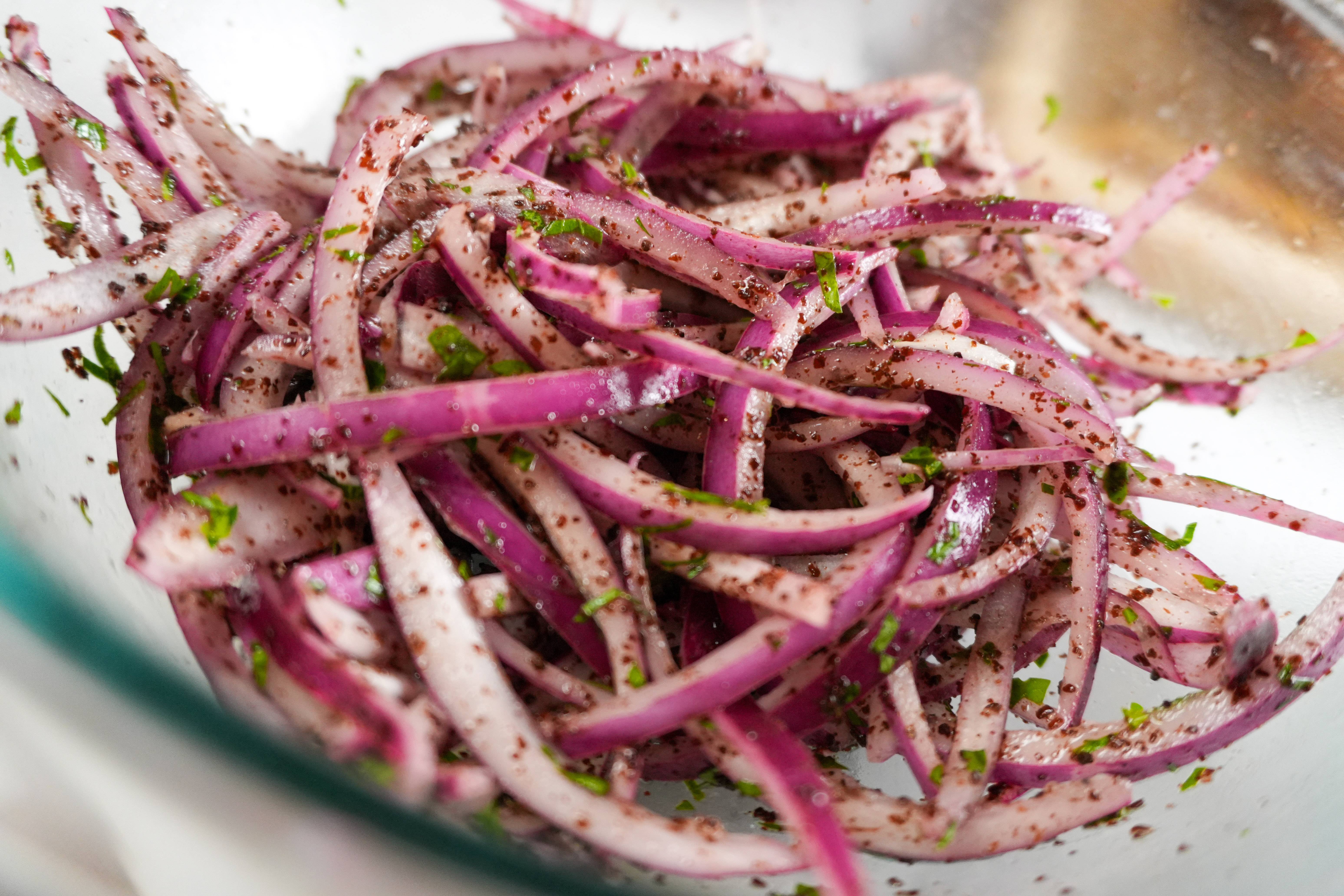 close up of sumac marinated red onions in a glass bowl.