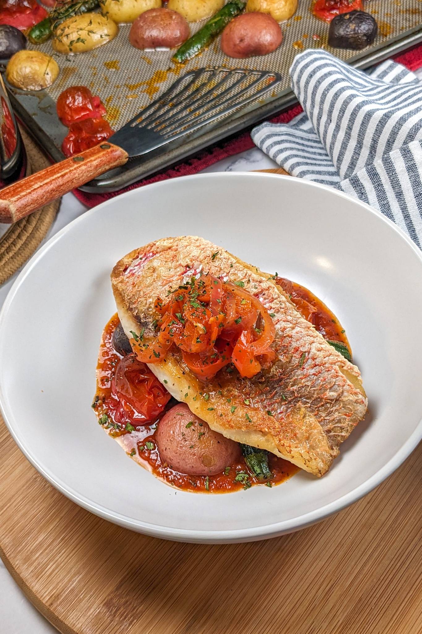 seared snapper fillet on a bed of roasted vegetables and haitian creole tomato based sauce and topped garnished with sauteed onions.