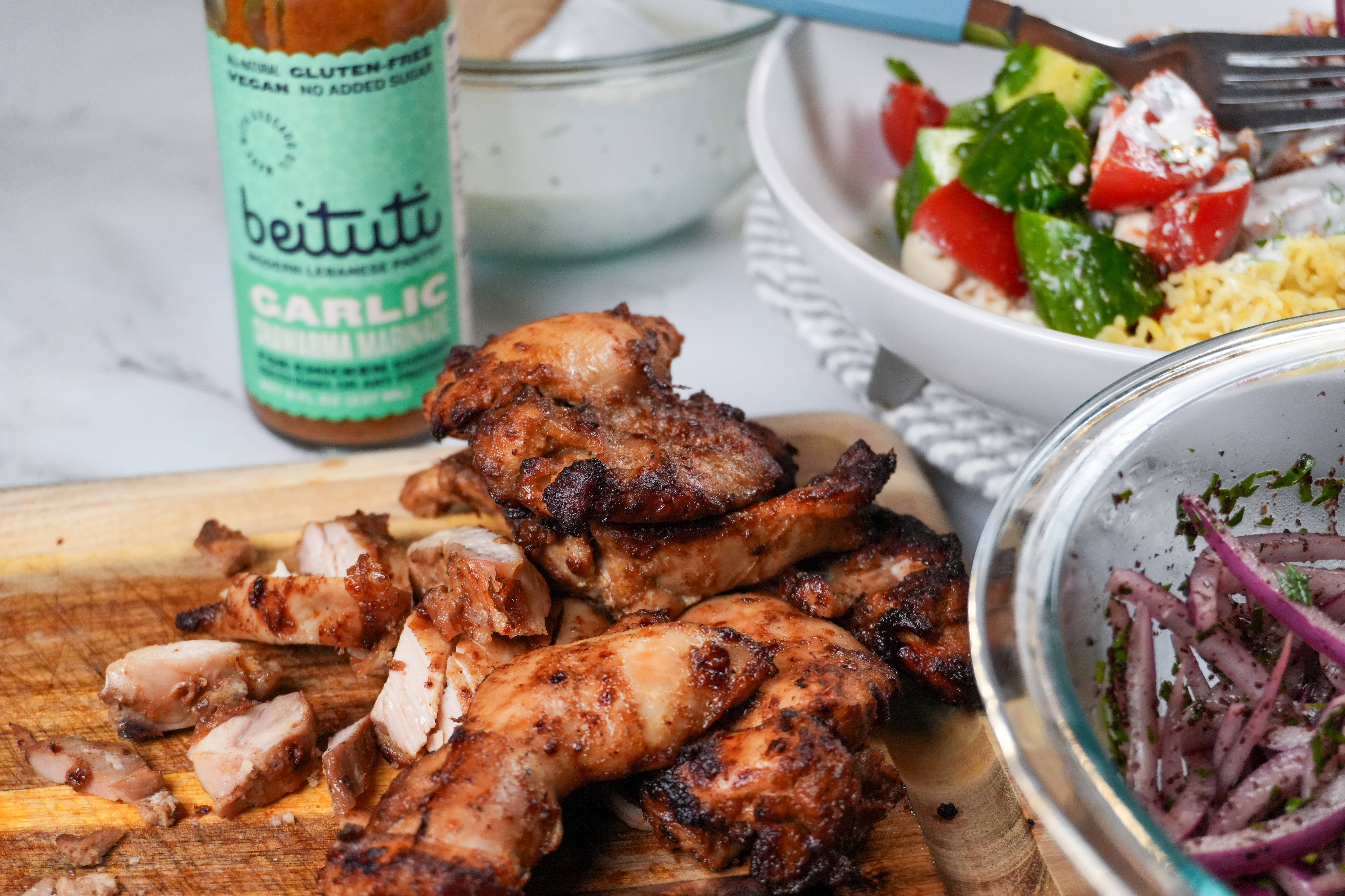 Air fried shawarma marinated chicken on a cutting board next to a bottle of Beituti Garlic Shawarma Marinade.