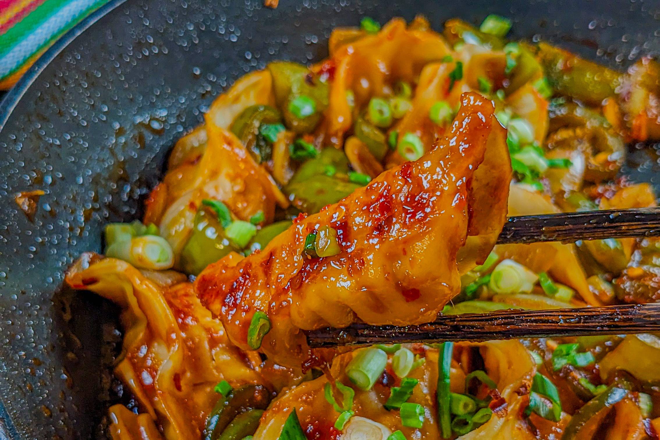 ones seared and glazed dumpling held between a pair of chopsticks.