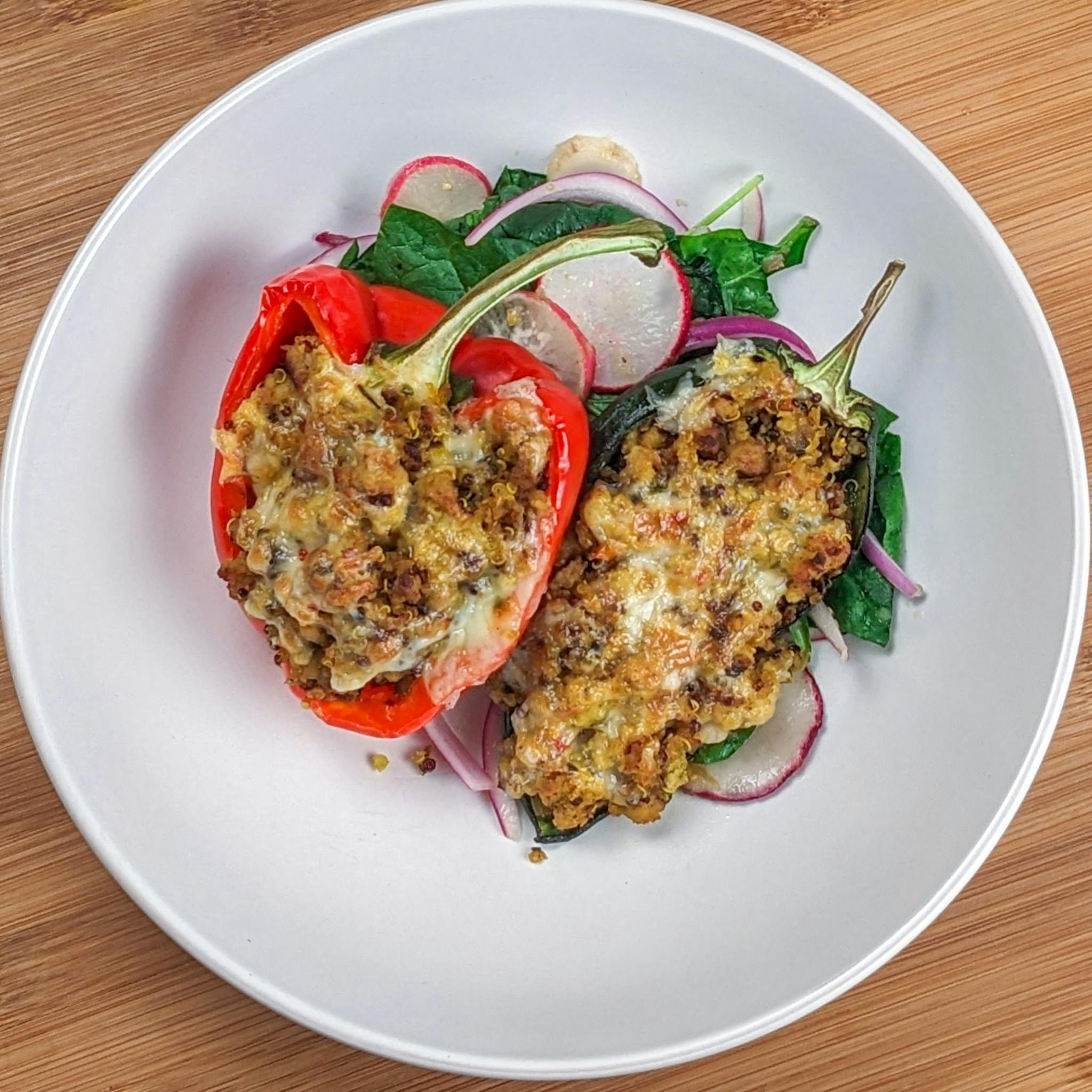 Baked stuffed bell peppers and poblano peppers with ground turkey and quinoa with melted pepper jack cheese on a bed of greens with sliced radishes and red onion.