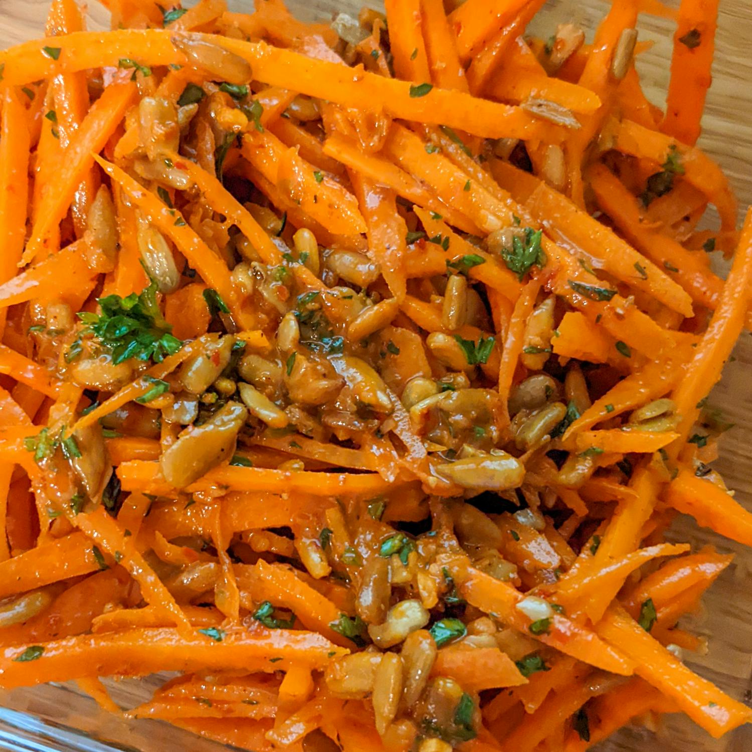 close up of shredded carrot salad with harissa, seasoning, fresh chopped parsley and sunflower seeds.