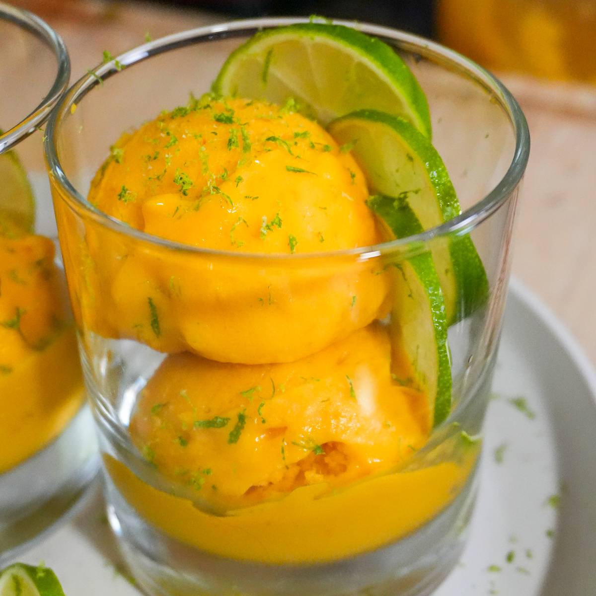 mango coconut felato getato style in a glass cup garnished with lime slices and zest.