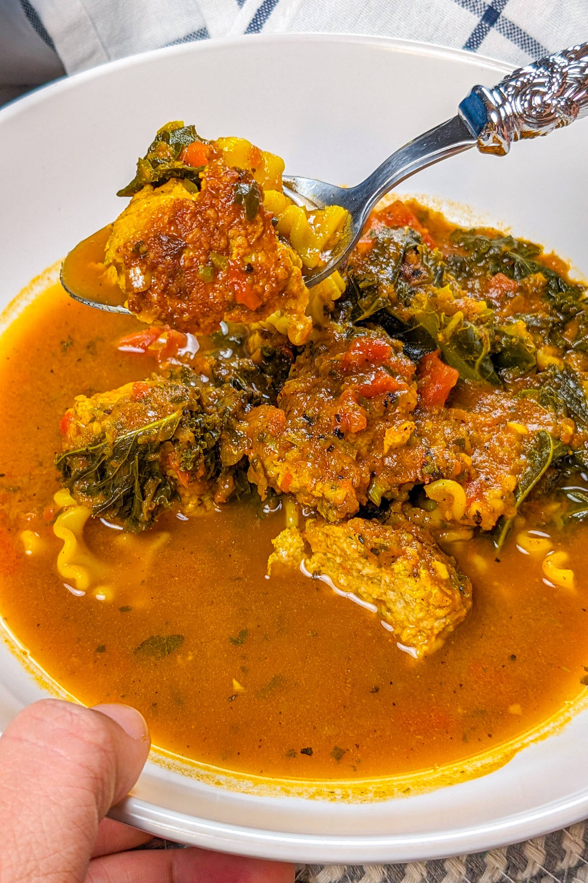 One-Pot Curry Meatball Soup with Ground Turkey and Kale om a wide rim pasta bowl with a spoon.