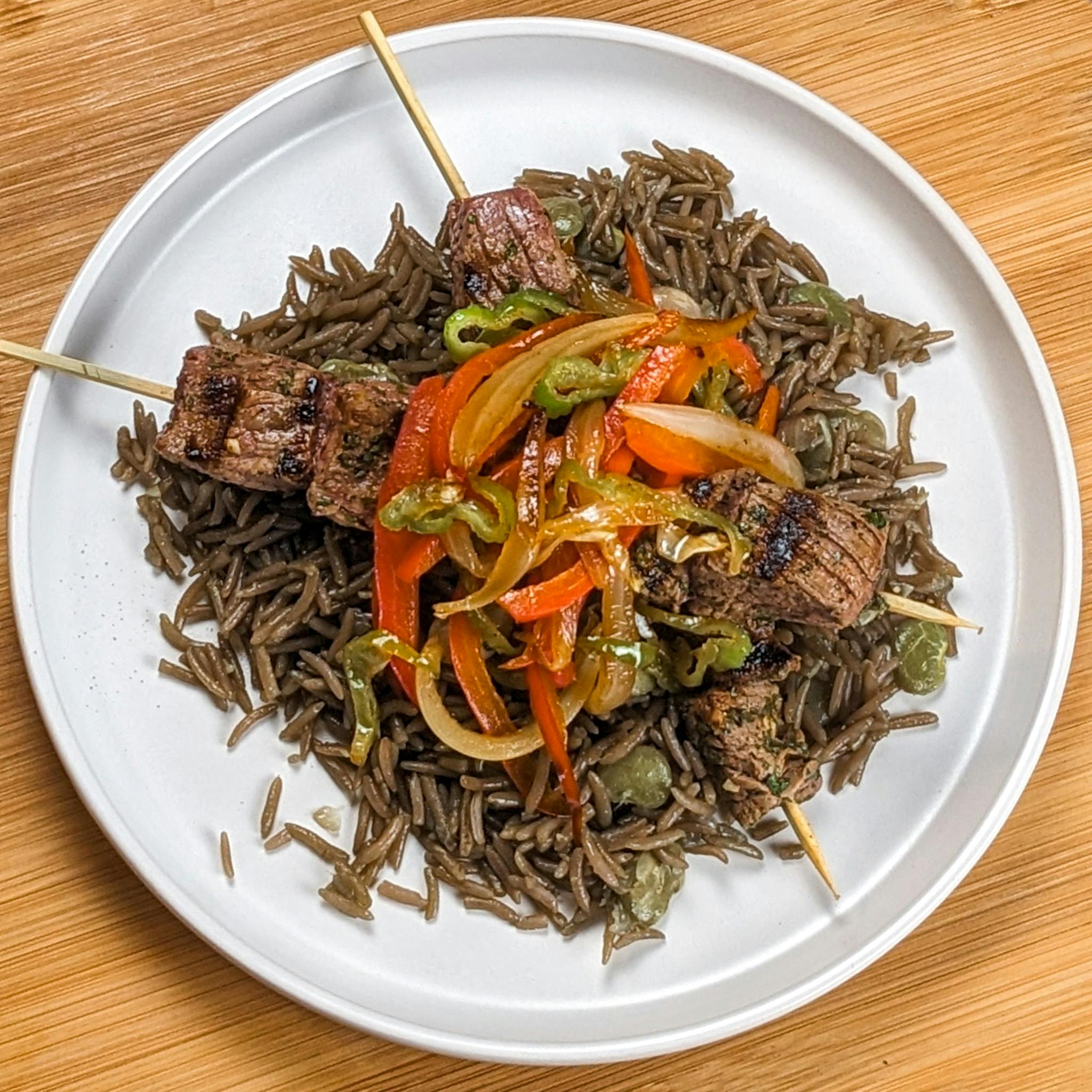 Top view of the Grilled beef skewers with (Djon Djon) black mushroom rice with escovitch-style spicy sauteed vegetable slaw on a flat round plate.