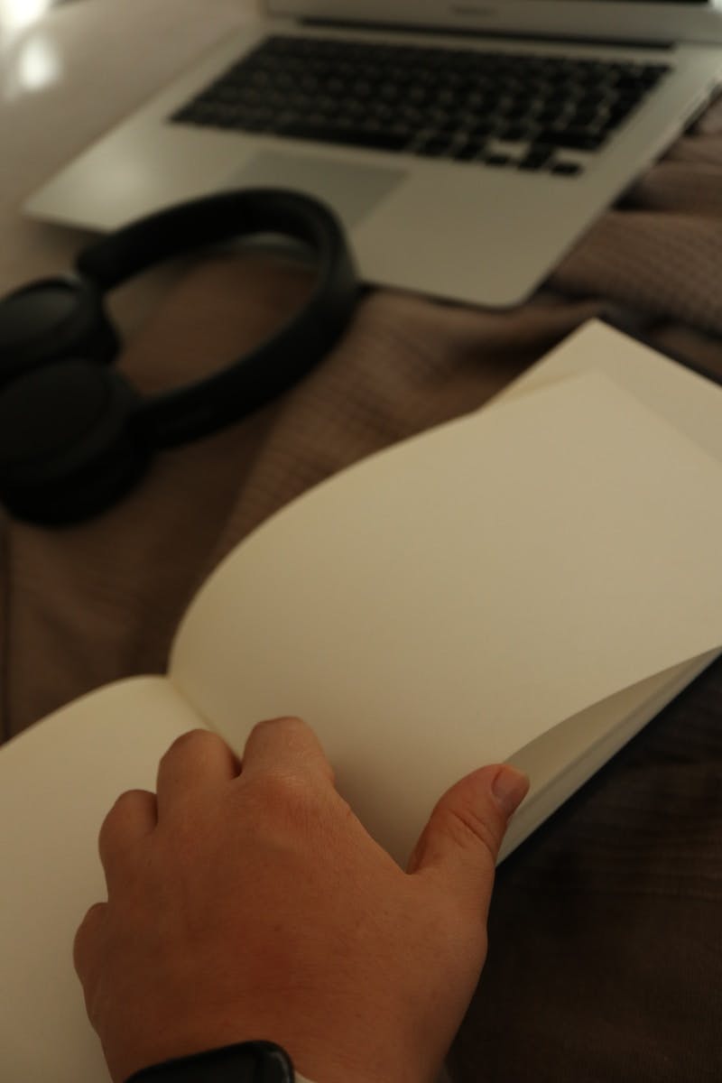 A person reading a book in front of a laptop