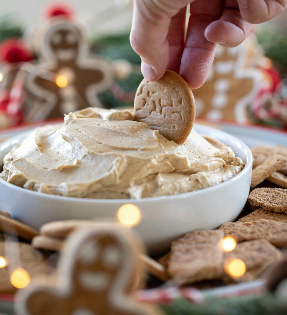 hand with gingersnap taking a scoop of gingerbread dip. 
