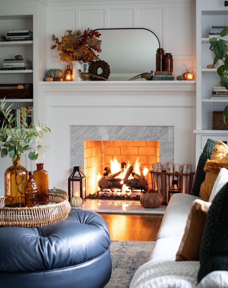 fireplace decorated for fall in a living room with ottoman and sofa.