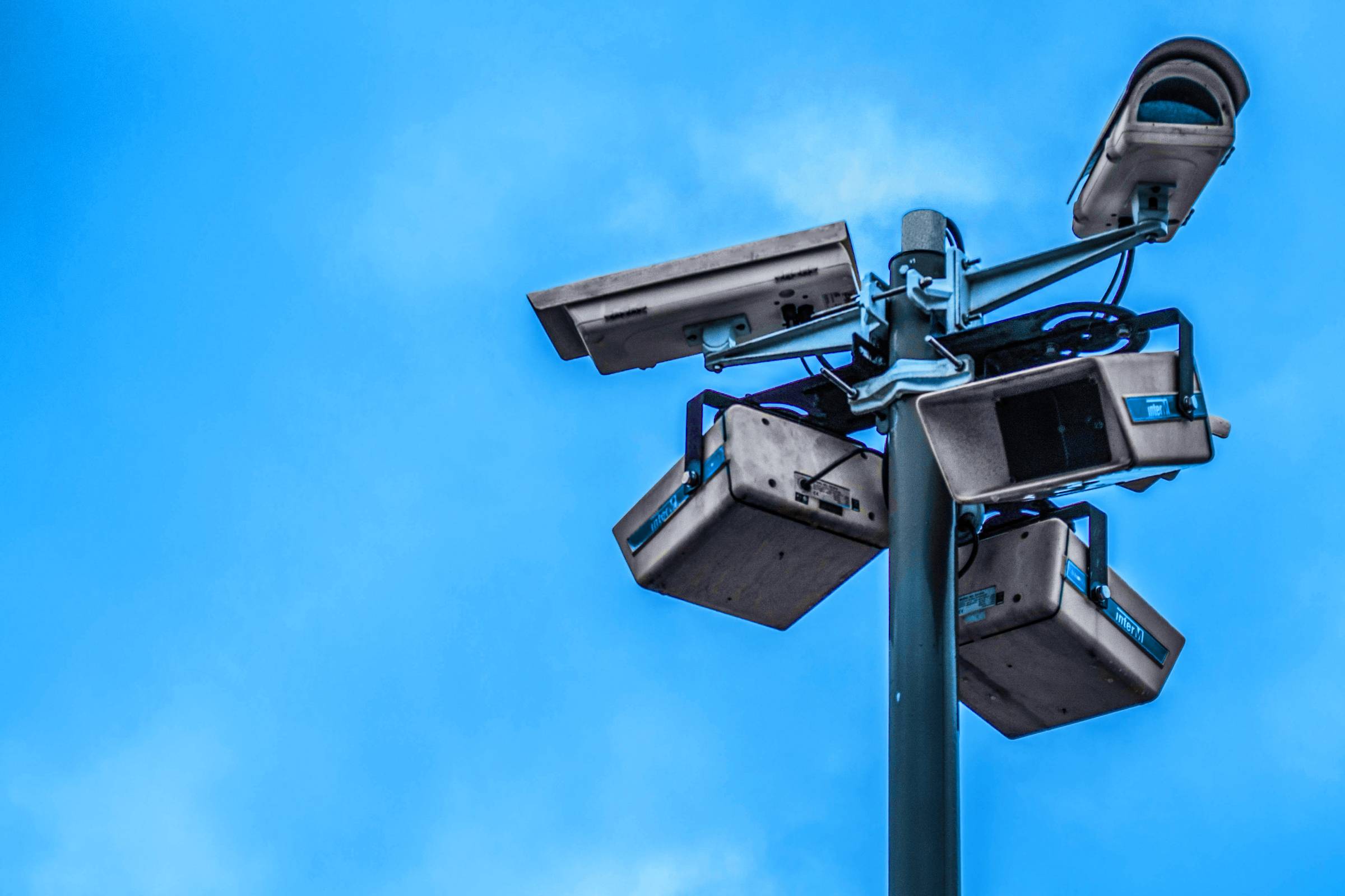 Image of security cameras against a blue sky.  Image thanks to Nathanial Dahan on Unsplash.  