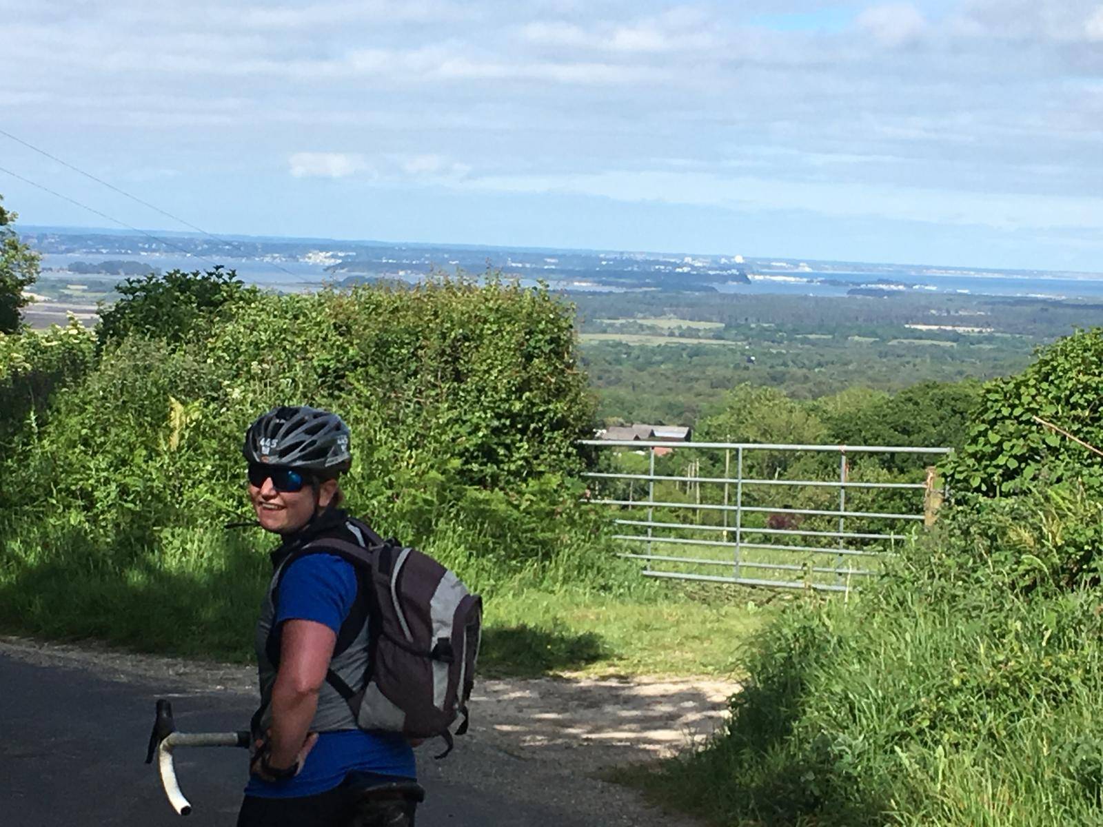 Image of Sheela Hobden wearing a cycling helmet, with views from the Purbecks to Poole harbour behind.  She has stopped cycling for the photograph.  www.bluegreencoaching.com