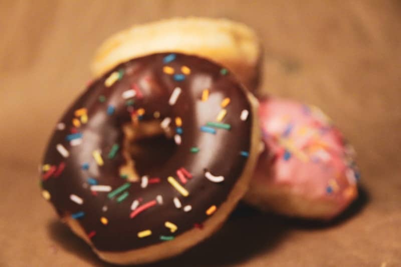 Three delicious donuts with sprinkles on a brown background.