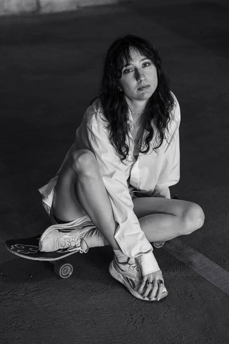 Woman in oversized shirt sits on skateboard