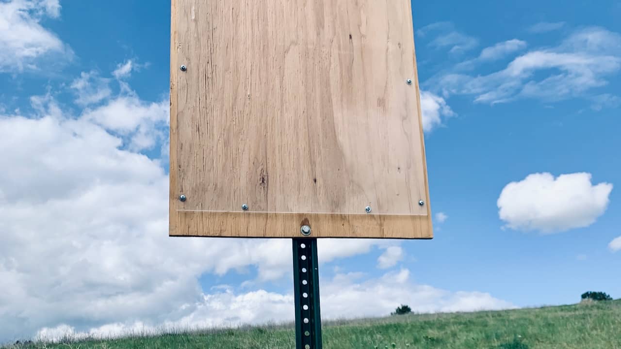 an empty sign on a trail in front a blue sky with puffy clouds