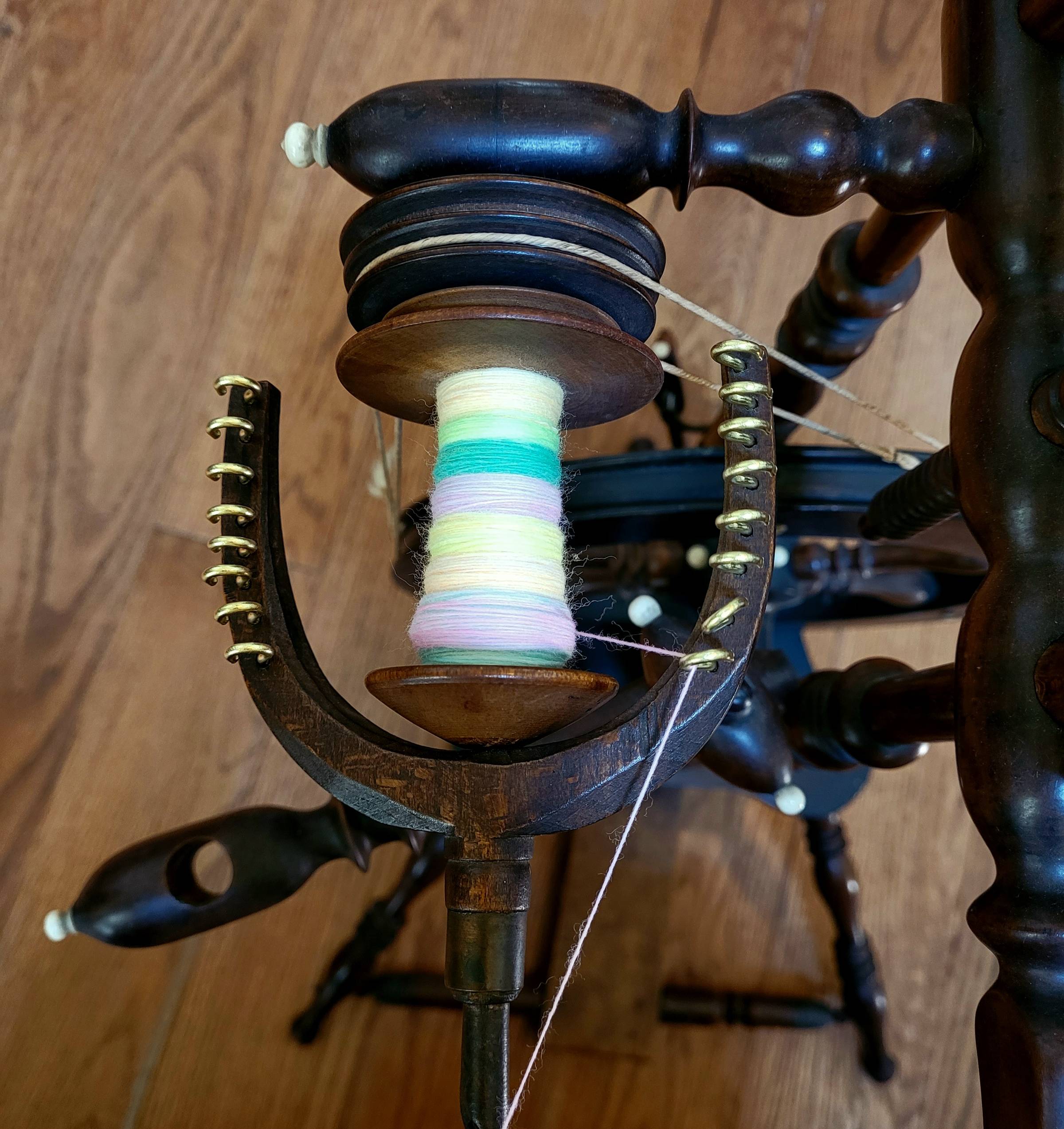 Neon/pastel rainbow single-ply yarn on the bobbin of a dark-stained, antique flax spinning wheel.