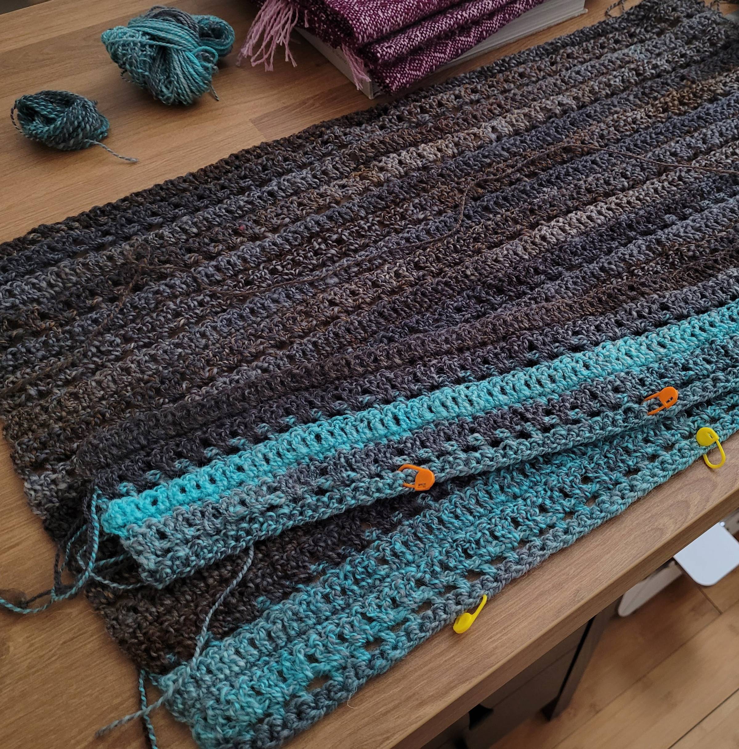 One large crocheted panel with a sky blue/gray marled stripe at the bottom, and the remainder being gray/brown marled. A partial second panel is laying on top of the first one.