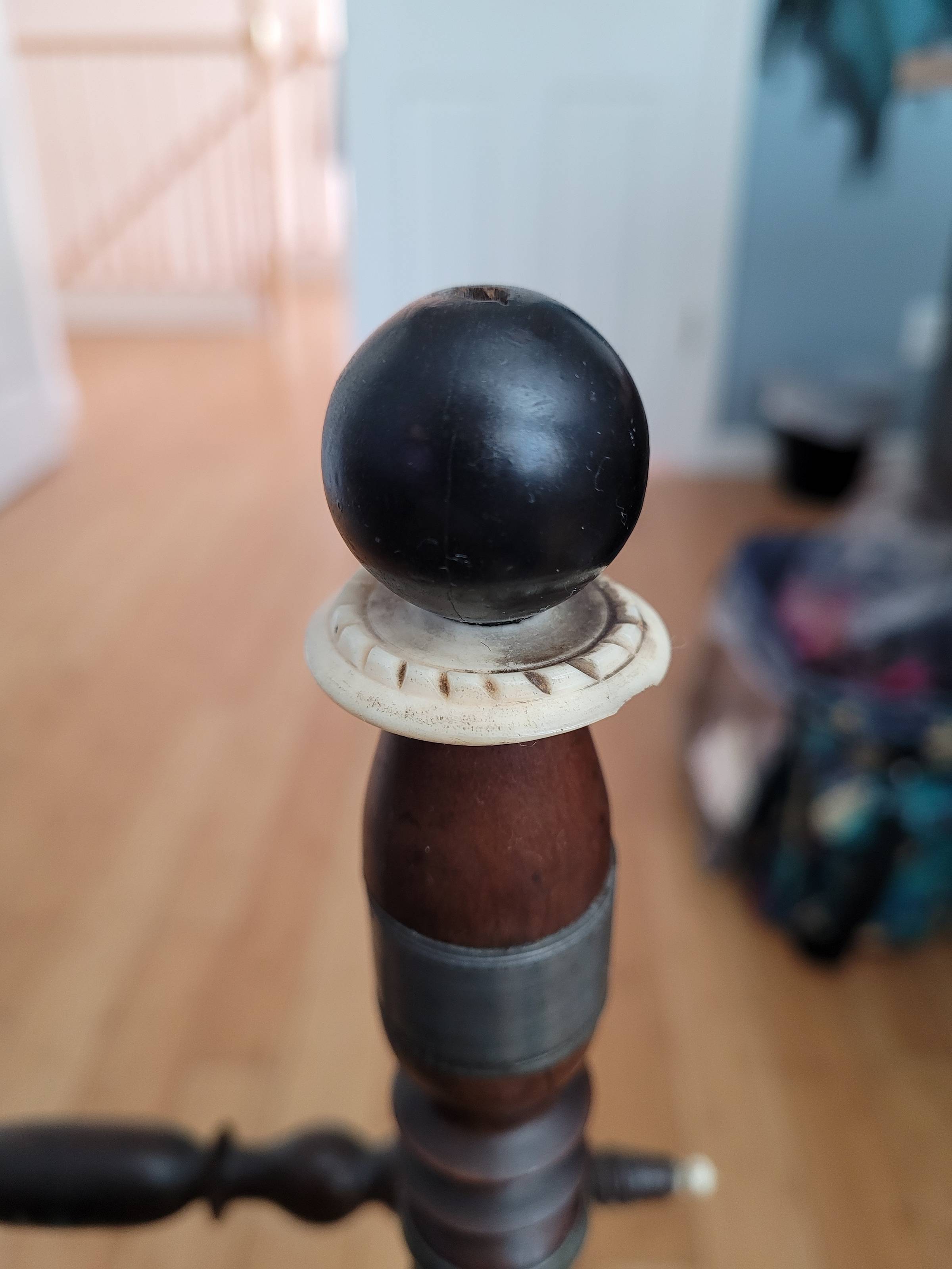 Part of the detailing on an antique flax spinning wheel: bone/horn decorative disc and black, painted ball topping the tension handle. The bone/horn detail is in the process of being cleaned.