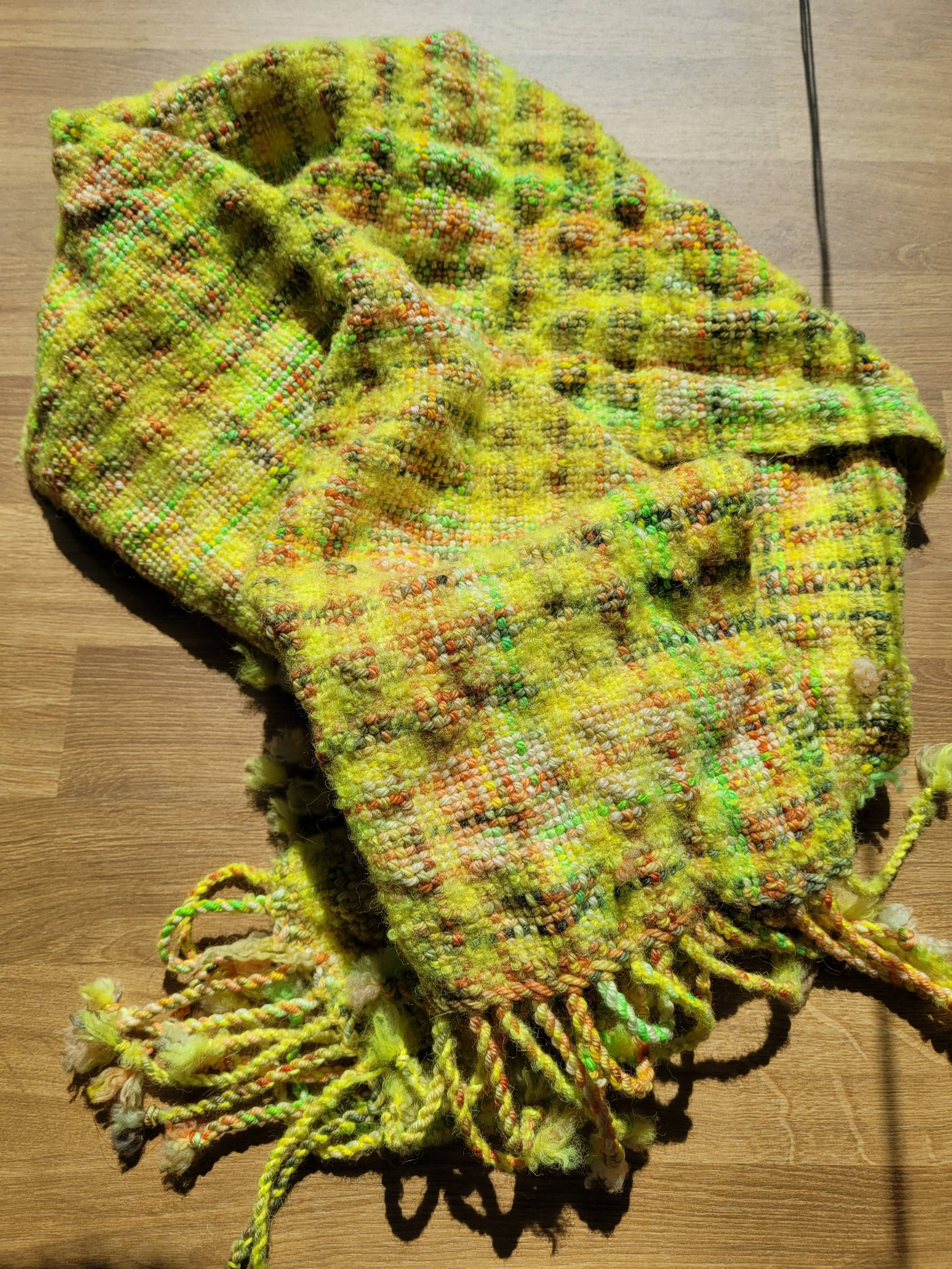 Mostly-yellow plaid scarf with variegated yellow/green/orange blips throughout. Scarf has experienced differential shrinkage, so parts of it are felted and puckered compared to others.