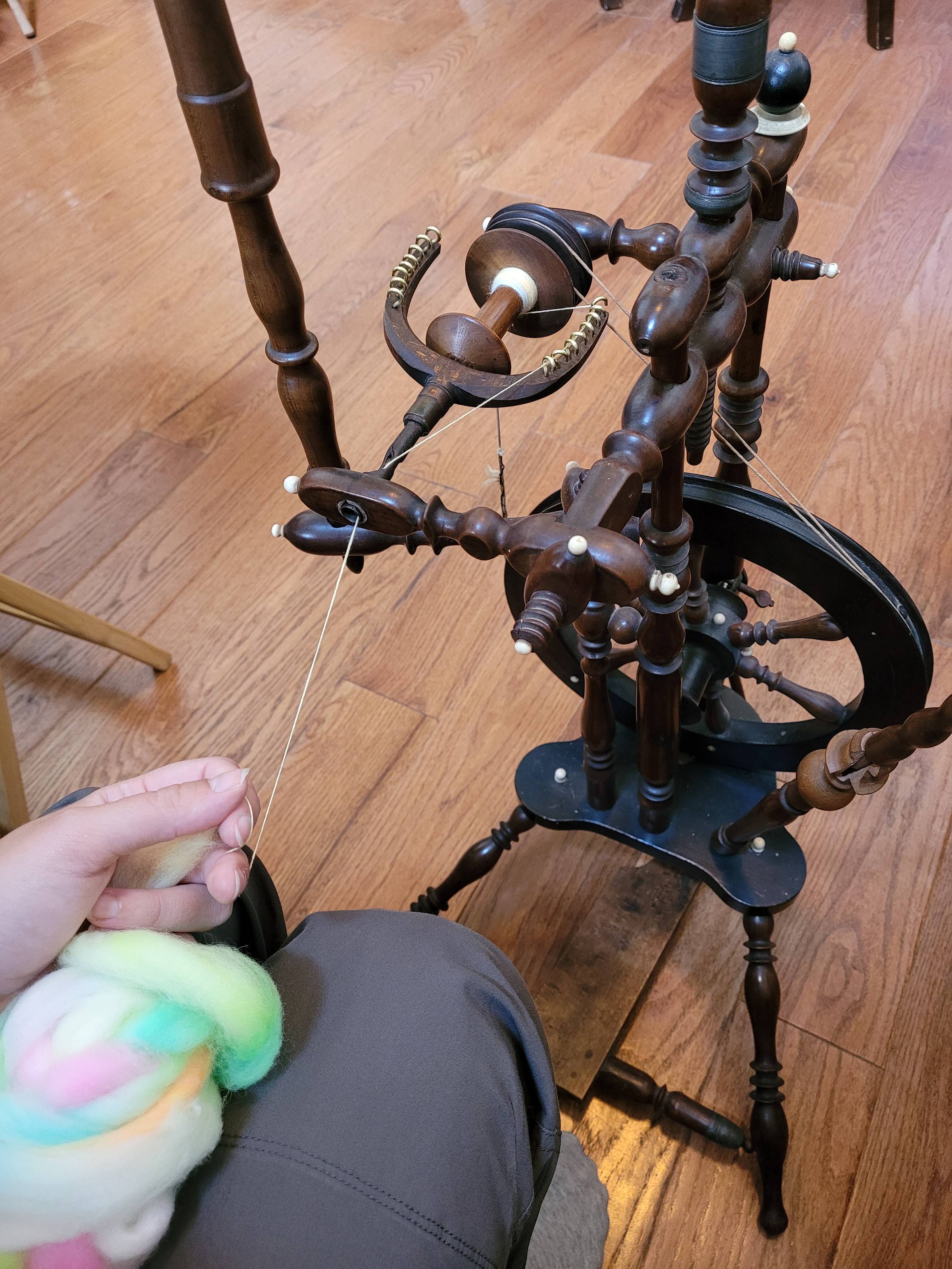 Neon/pastel rainbow fiber being spun into yarn on a dark-stained, antique flax spinning wheel.
