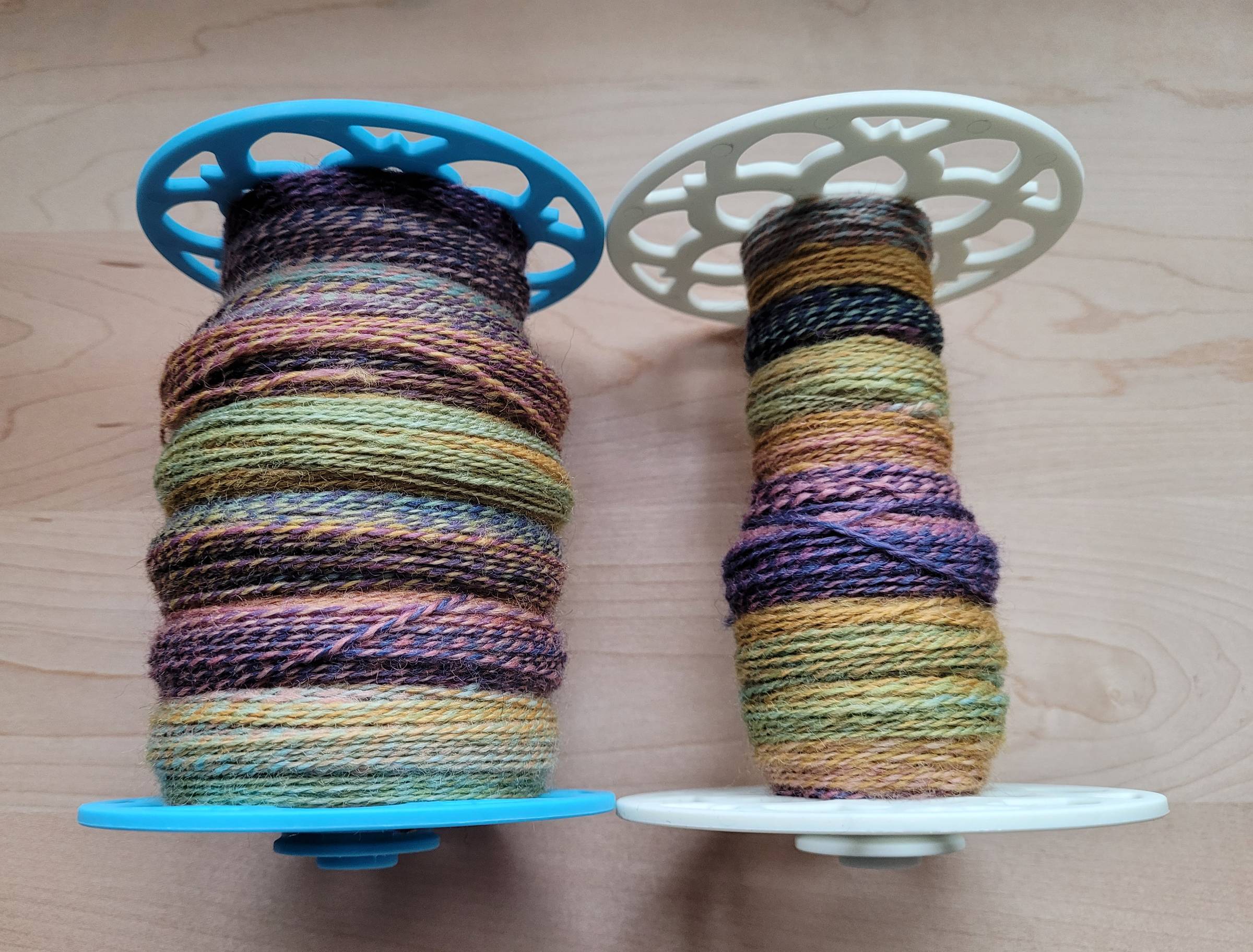Two plastic bobbins with multicolored, plied yarn.
