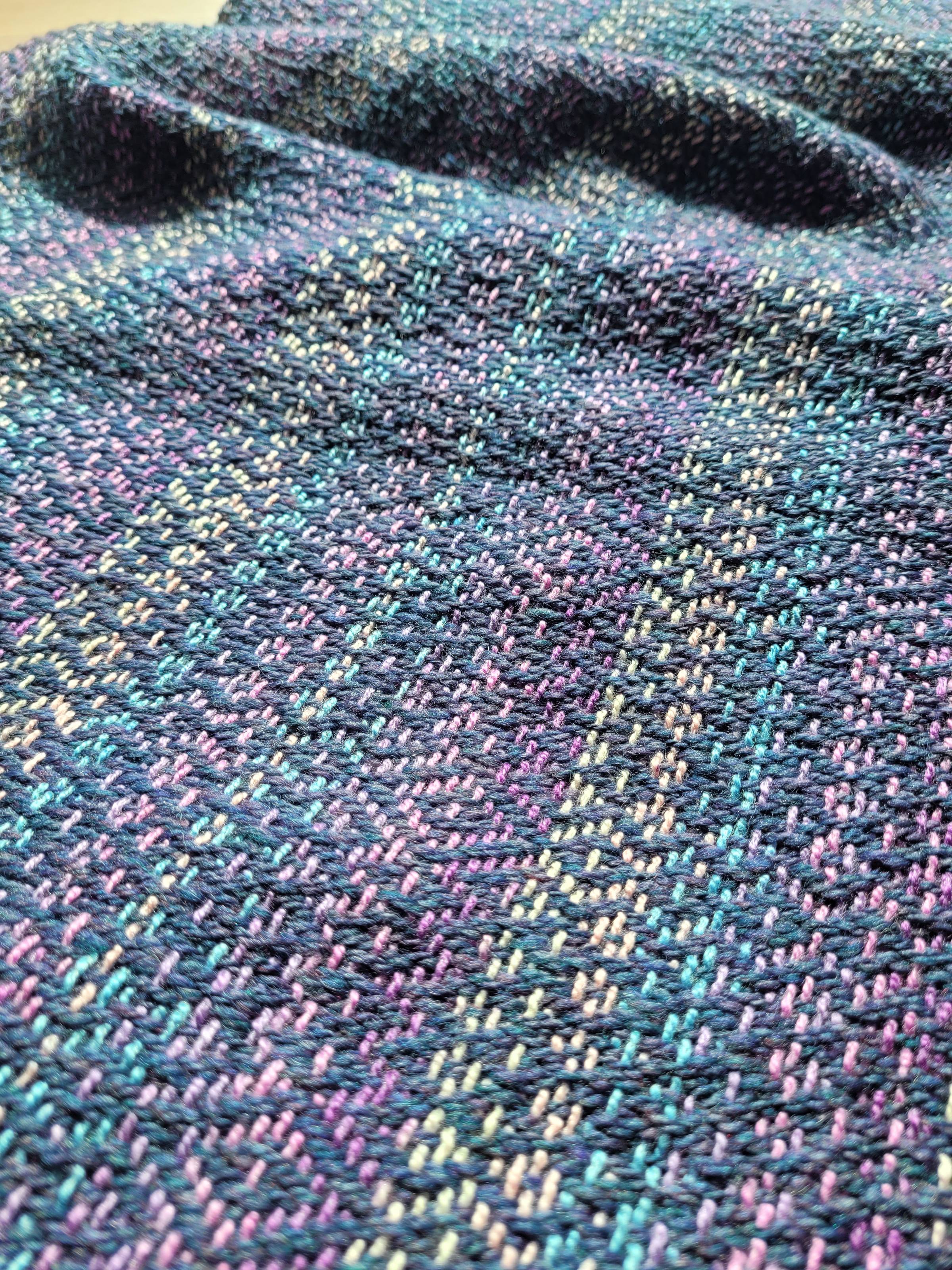 Handwoven fabric  in a diamond twill pattern; warp: lilac, sky blue, and cream stripes, weft: dusty blue handspun yarn. This image is a closer detail shot than the one above.