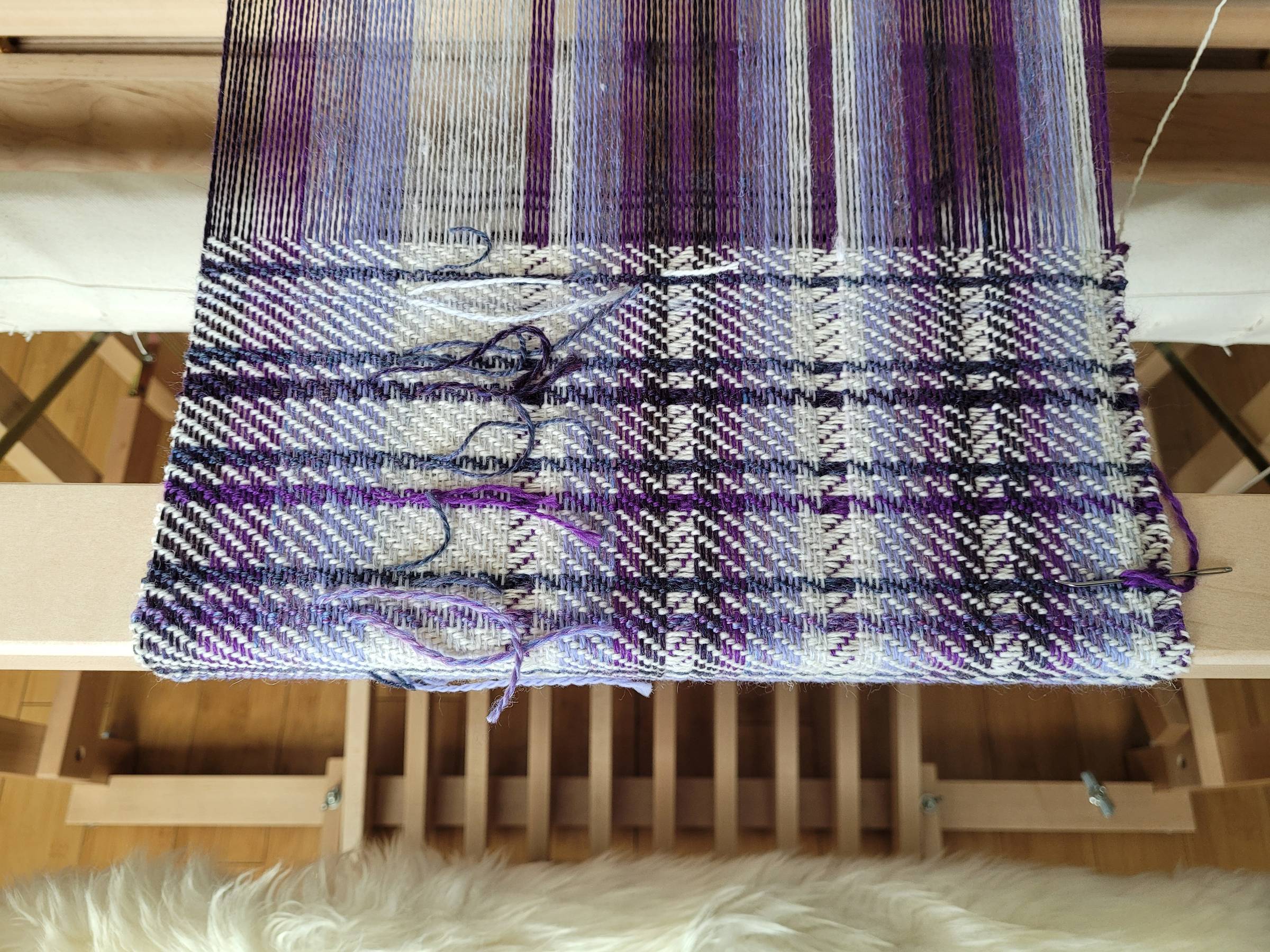 Striped twill weaving project using various shades of purple contrasted with white. Many ends are visible from the short stripes.